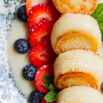 Soft and fluffy syrniki stacked with powdered sugar and fresh berries on a plate