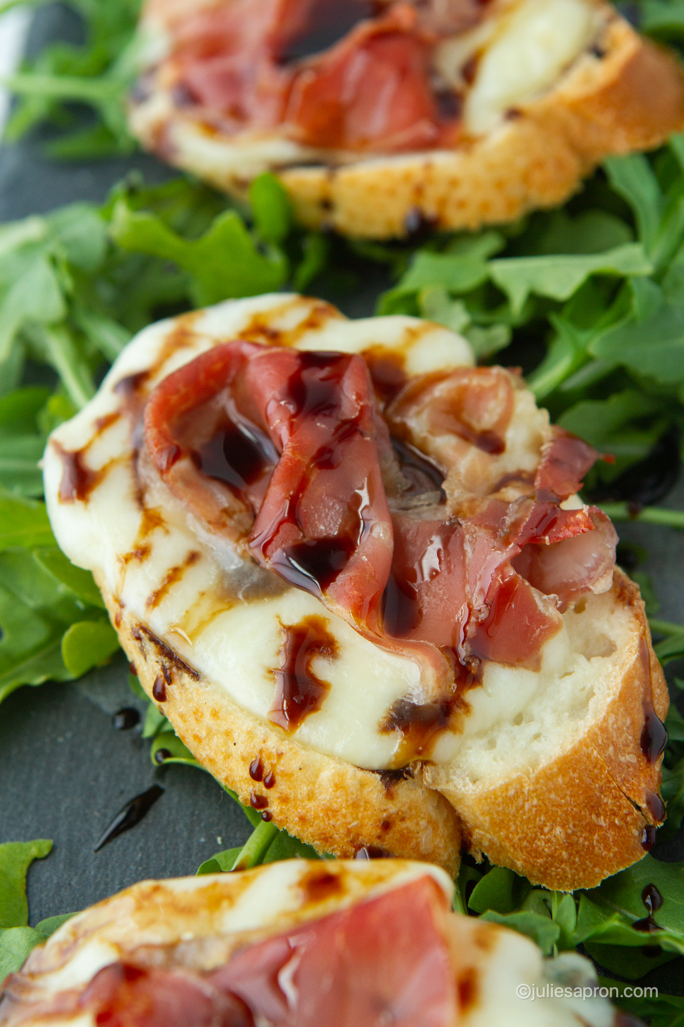 close up of prosciutto melts on arugula