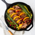 cast iron skillet with pork tenderloin and oranges and cranberries