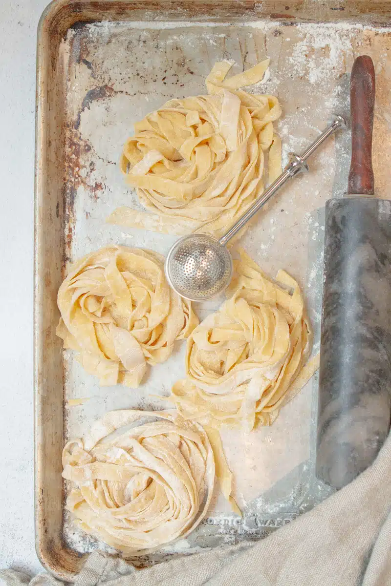 Homemade pasta without pasta machine ingredients including flour eggs olive oil and salt on a light neutral background